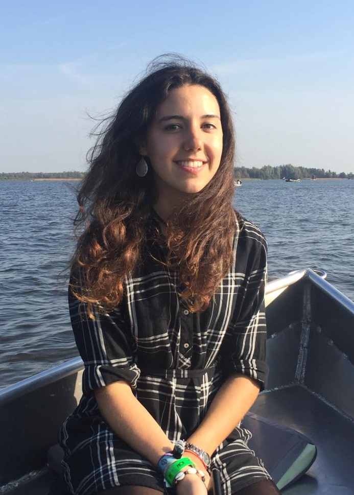 Fotografia de mí en una balsa en un lago, estoy sonriendo y mirando a la camara con una camisa a cuadros y el pelo suelto.
